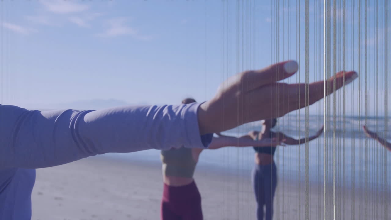 On beach, people practicing yoga with focus on extended hand in foreground