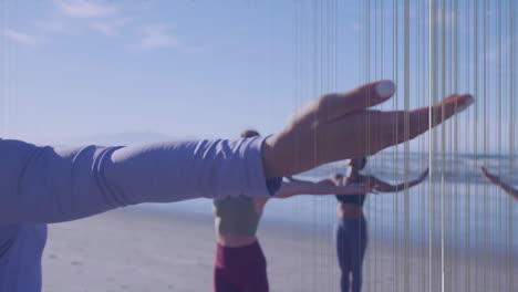 on beach, people practicing yoga with focus on extended hand in foreground