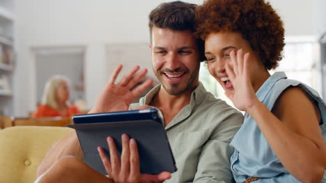 pareja sonriente en casa en el sofá haciendo una llamada de video en una tableta digital