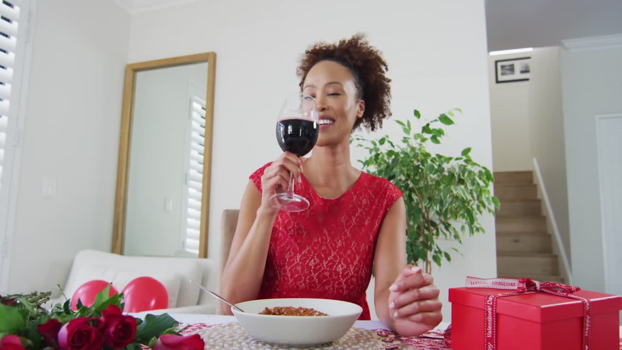 Mixed race woman on a valentines date video call, drinking wine