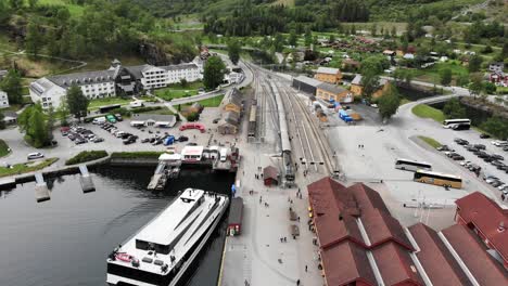 Aerial:-flying-over-the-Flåm-harbour-among-mountains,-over-the-town-and-the-station