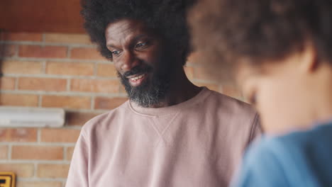 middle aged black father and his pre teen son standing at a workbench in their garage building a racing kart together, low angle, close up, selective focus, focus on dad