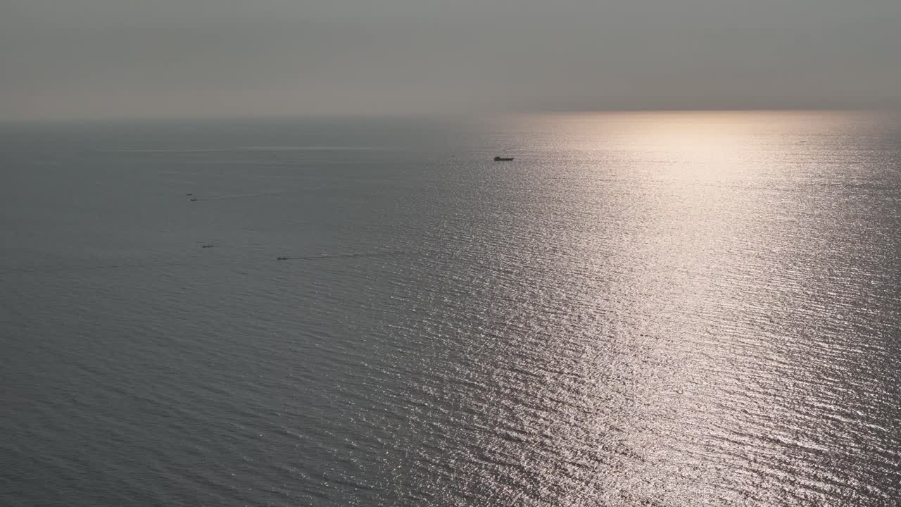 A captivating aerial shot captures a small, solitary boat in the middle of a vast, tranquil ocean. The drone footage provides a high-angle view of the deep blue water