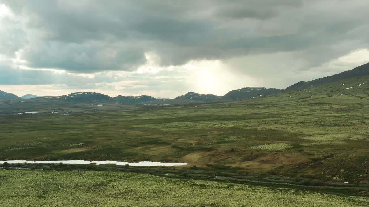 panorámica aérea que se eleva sobre las llanuras de pastizales del parque nacional de rondane, condado de innlandet, noruega, mientras la luz del sol se rompe entre las nubes