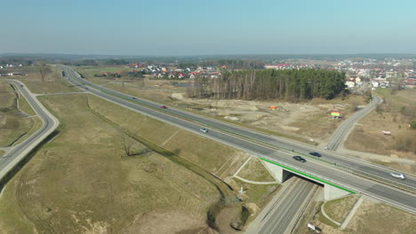 aerial shot of a highway intersection with overpass, vehicles in transit, and surrounding early spring landscape