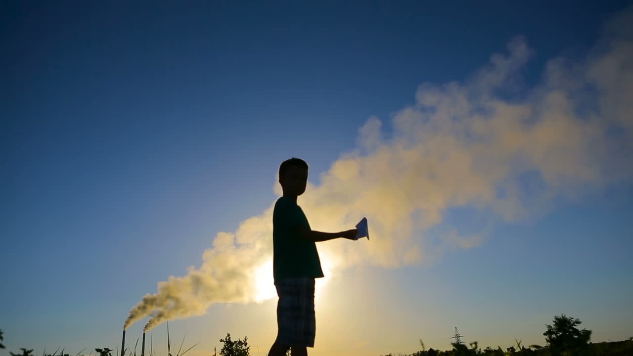 Boy With Origami Plane. Young boy playing a paper airplane near smoky pipes
