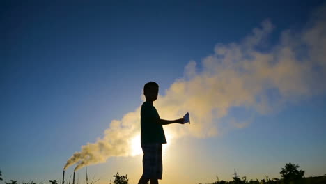 boy with origami plane. young boy playing a paper airplane near smoky pipes