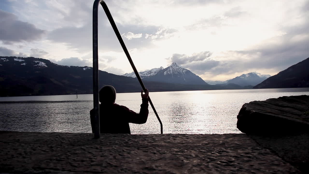 silueta de un hombre sentado frente a un lago maravilloso mientras observa la puesta de sol