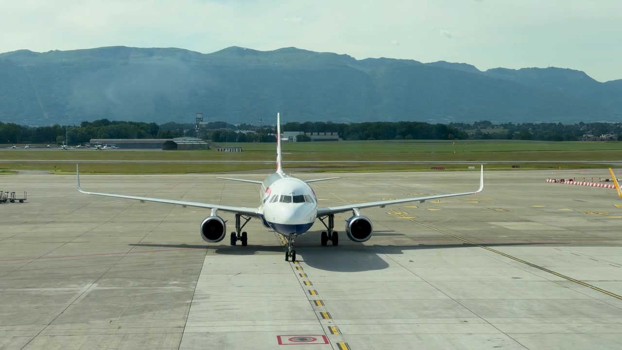 Vista frontale di un aereo di linea che rulla lentamente su una pista, sullo sfondo di montagne panoramiche.