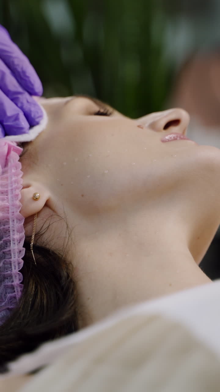 Beauty clinic. Beautician hands in gloves making face anti-aging injection in a female neck. A woman gets beauty facial cosmetology procedure. Botox. Vertical video
