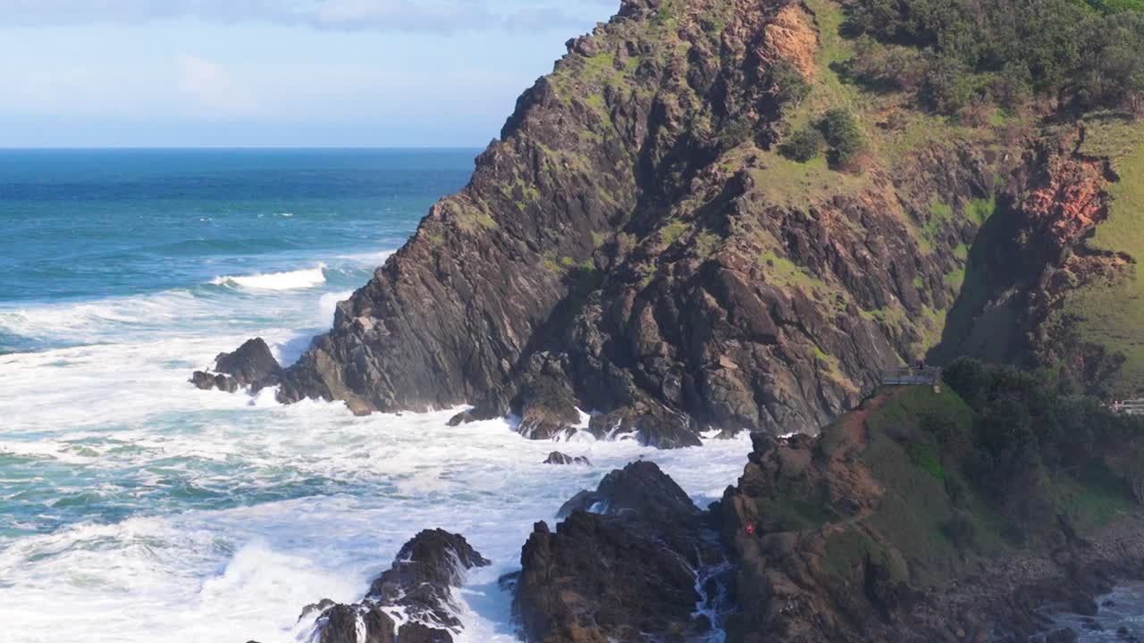 Dynamic ocean waves crash against rugged cliffs under bright sunlight, showcasing nature's power and beauty in Byron Bay, Australia