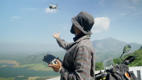 a young indian man landing his mini drone in a wild forest landscape of western ghats, india