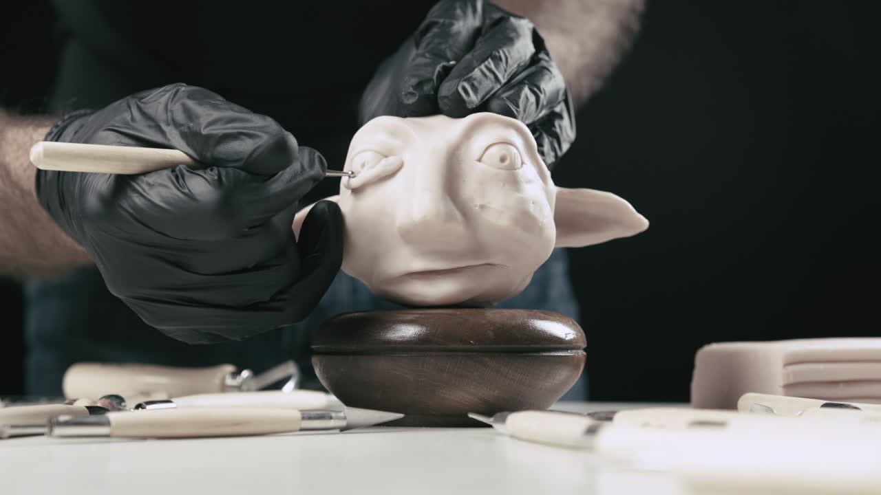 Artist models a plasticine puppet head's eye with a needle tool