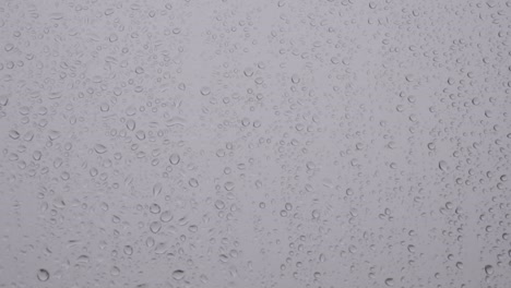 droplets of rain slowly roll down window pane, static closeup background