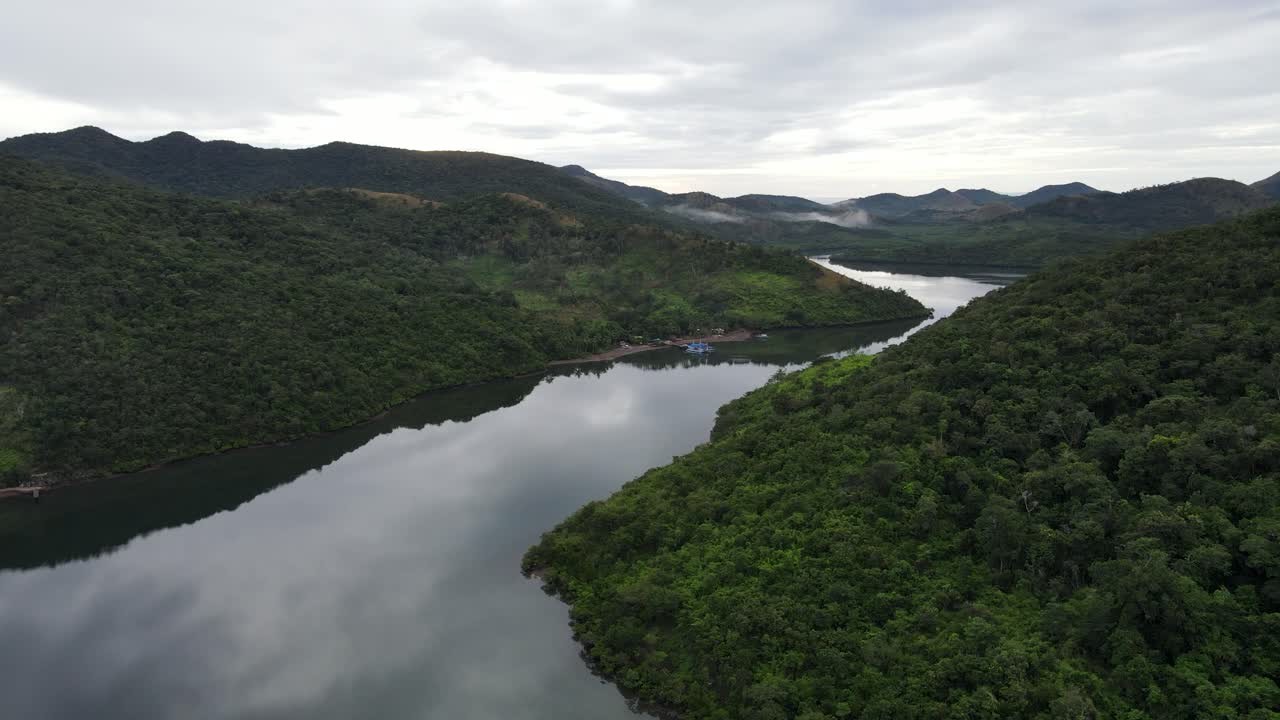 Aerial view of serene ocean river and lush hills in Culion island, Philippines. The mirror-like water reflects the overcast sky and nearby small Filipino village blends harmoniously with the landscape