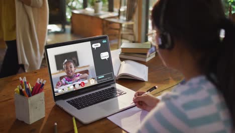 Composite-video-of-girl-using-laptop-for-online-lesson-at-home,-with-girl-raising-hand-on-screen