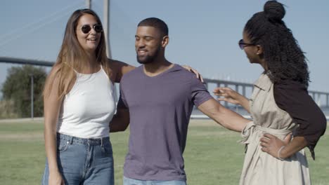 two female friends kissing african american man on meadow.