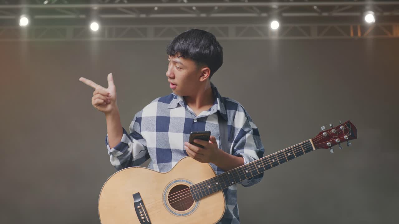 스마트폰을 사용하고 무대에 서서 을 가리키는 기타를 들고 있는 아시아 십대