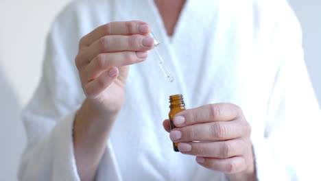 using dropper bottle, mature woman applying skincare serum at home in bathrobe