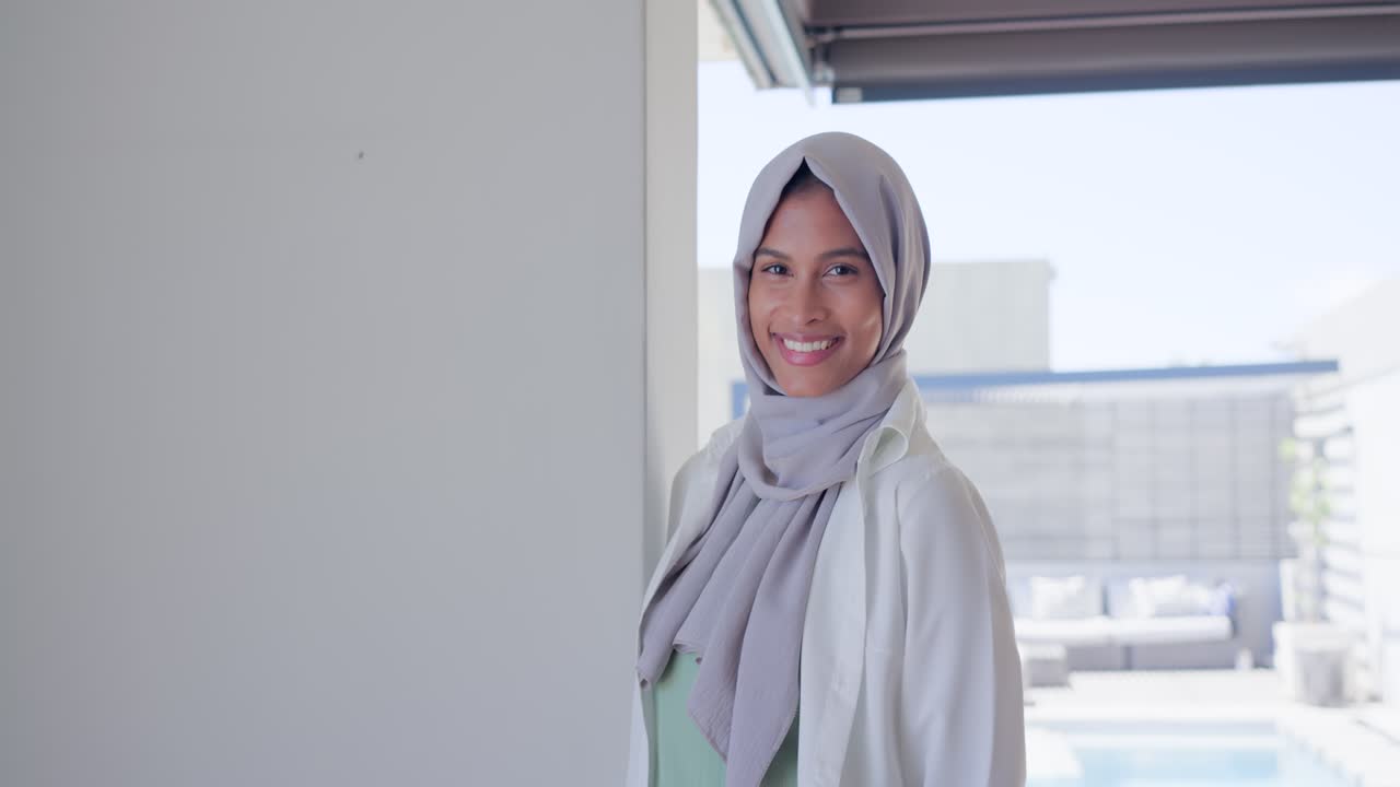 African American woman in gray hijab checking watch walking, leaning on pillar, laughing poolside