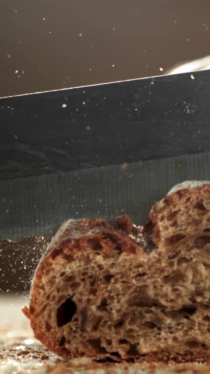 Close-up of a Serrated Knife Cutting Fresh Bread with Crumbs Flying