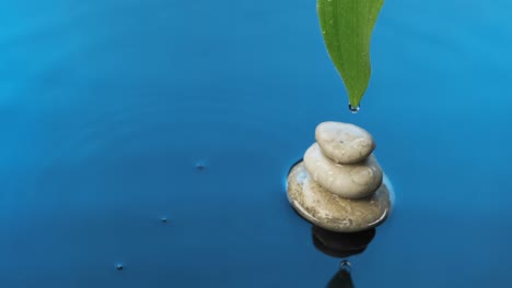 gotas de agua caen sobre la pirámide y hojas verdes en el agua azul. fondo del spa.