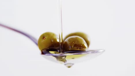 olive oil being poured on the olives held in spoon