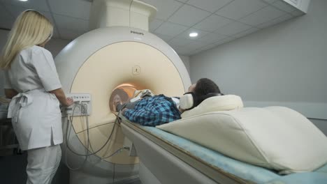 woman doctor makes knee-joint mri scanning. young man patient on automatic mri table enters into a closed-type magnetic resonance imaging machine using noise isolation headphones. modern equipment, coil on the patient's knee.