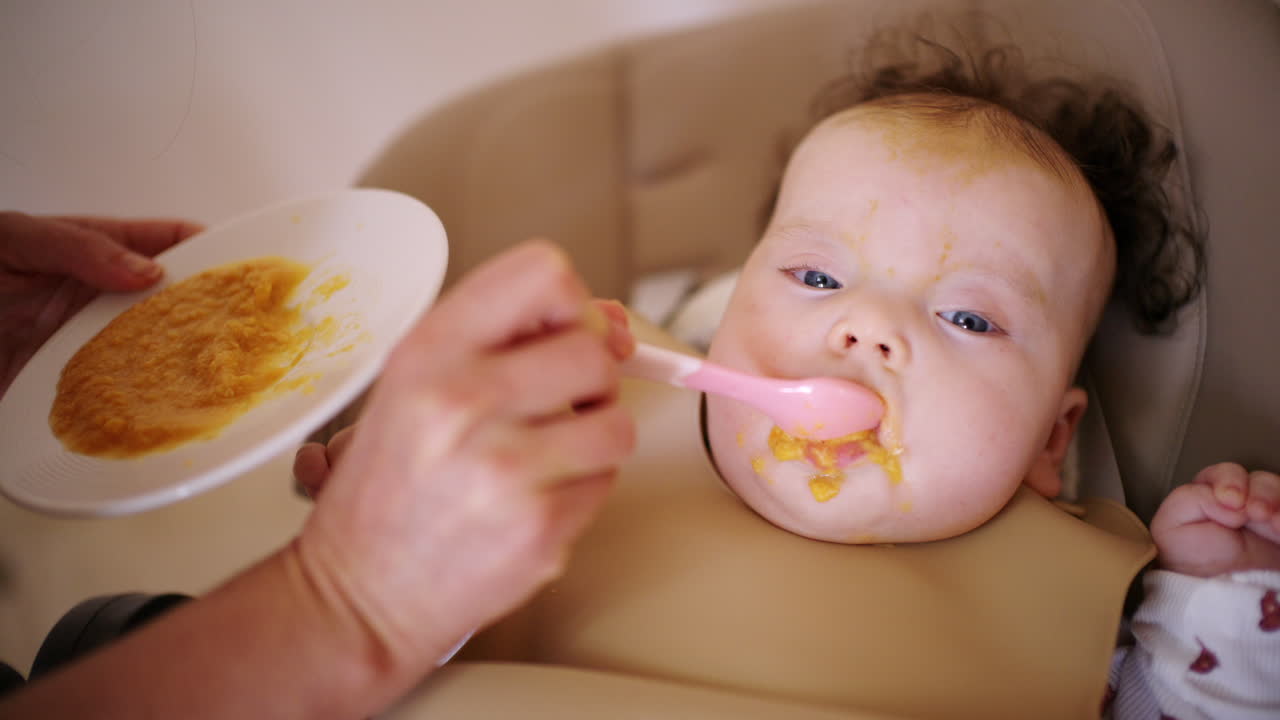 ハイチェアに座る赤ちゃんに大人がスプーンで離乳食を与えている。