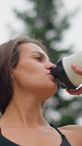 close-up of woman smiling while drinking water from a white water bottle, displaying hydration and refreshment, perfect for promoting fitness, wellness, or healthy living