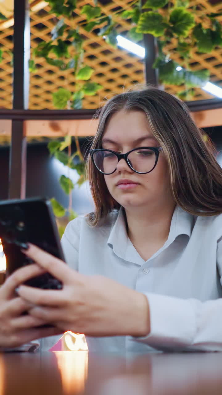 joven adulto sentado en un sentado de madera decorativo, operando el teléfono con una sonrisa sutil, en un restaurante bien decorado dentro de un bullicioso centro comercial, con una vibrante y animada atmósfera en el fondo