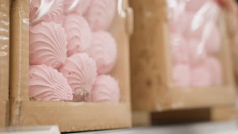 close up view of shopper placing pink swirl cookie carton on grocery shelf, capturing hand motion and texture, supermarket aisle shows bakery display, packaged treats selection