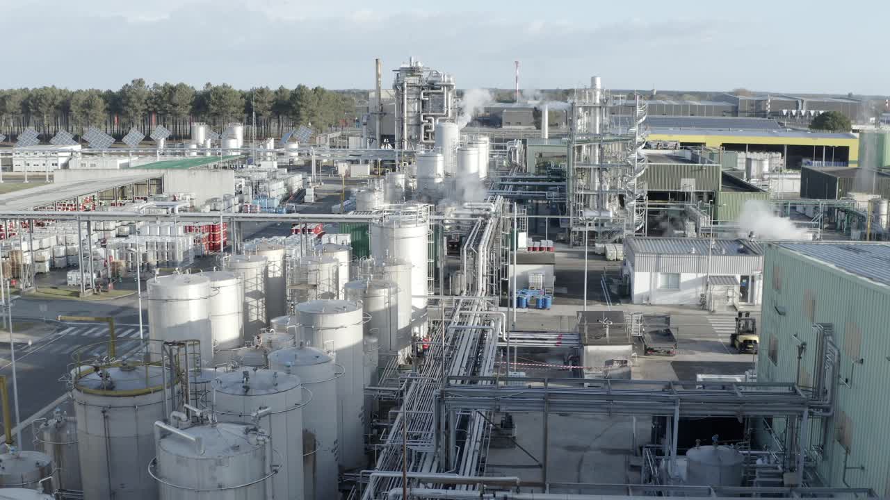 Aerial drone view through large industrial complex, showcasing numerous storage tanks, pipes, and steam emissions, Castets, France