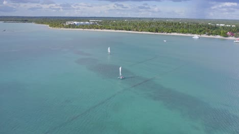 aerial orbiting shot of sailing catamaran on clear caribbean sea at playa nueva romana in summer