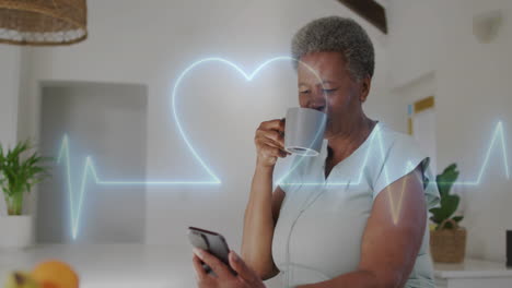 animación de cardiógrafo con corazón sobre una mujer biracial anciana usando un teléfono inteligente en casa