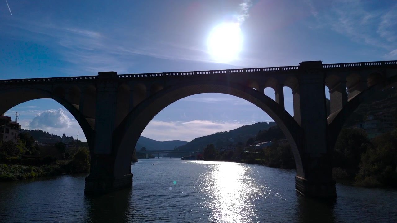 Dron volando sobre el río bajo un puente de piedra, escena del puente, el sol y el río