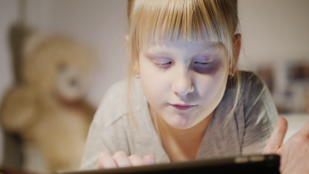 침실이 있는 태블릿을 즐기는 아이의 초상화는 저녁에 침대에 누워 있다