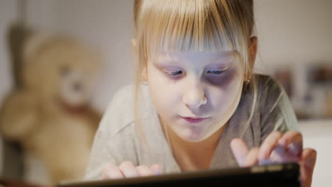 retrato de un niño que disfruta de una tableta con un dormitorio yace en su cama por la noche