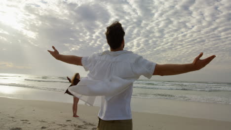 rear view of young couple standing with arms outstretched and looking at sea on the beach 4k