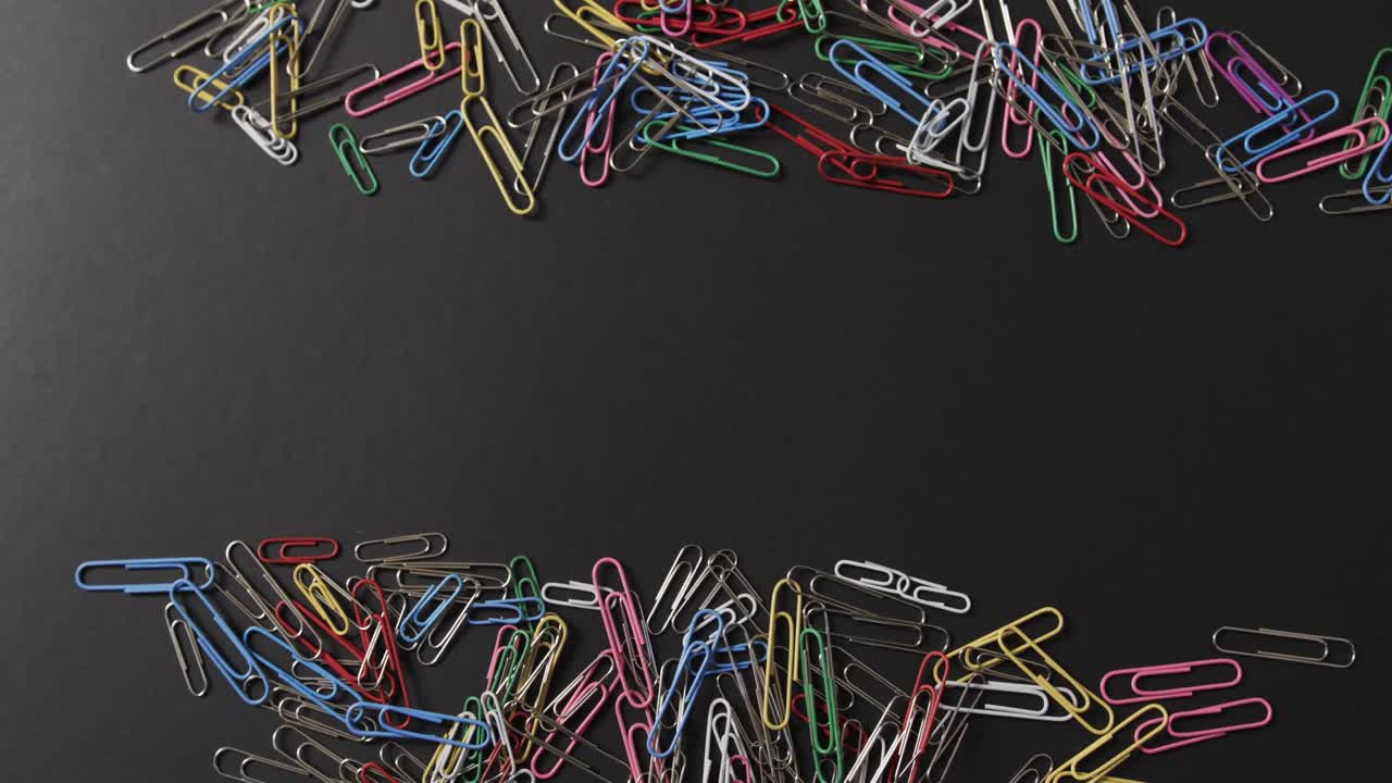 vista aérea de clips de papel de colores dispersos con espacio de copia en fondo negro, en cámara lenta