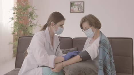 female doctor takes the pulse of an elderly patient sitting on a sofa