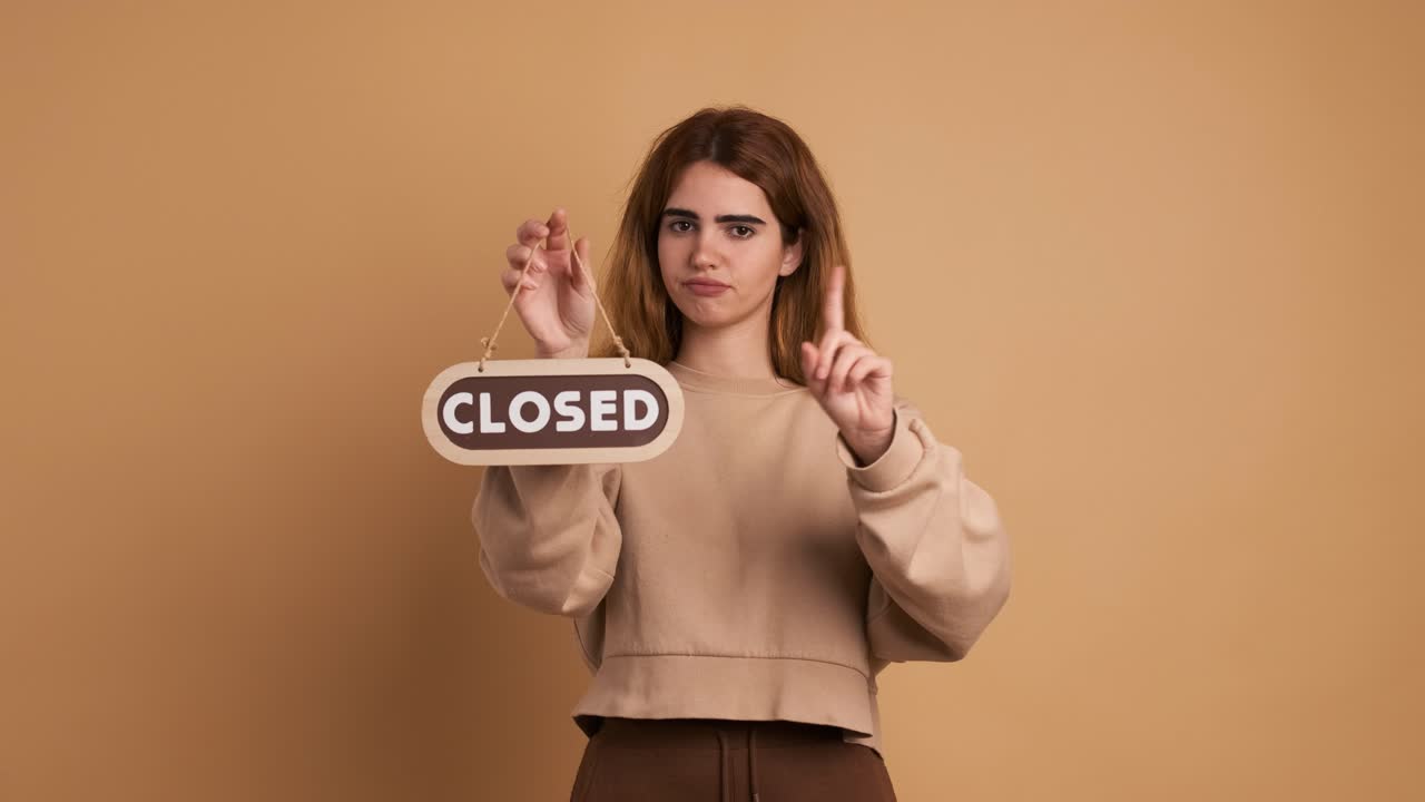 Young woman standing with closed sign near wall