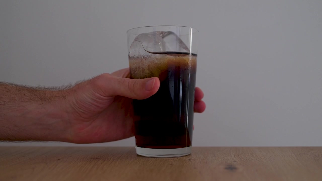 Un bicchiere di caffè nero freddo è appoggiato su un tavolo di legno mentre una mano si allunga per prenderlo