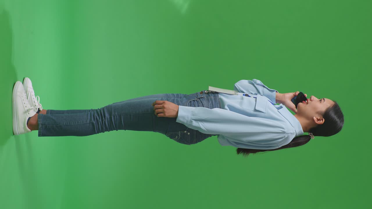 스튜디오의 녹색 화면에서 휴대전화로 이야기하는 아시아 사업가 여성의 전체 몸의 측면 시각