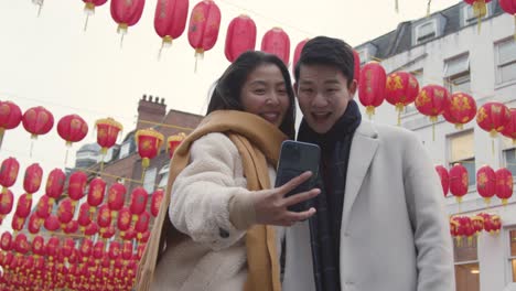 una joven pareja asiática de vacaciones posando para un selfie en un teléfono móvil en chinatown, londres, gran bretaña.