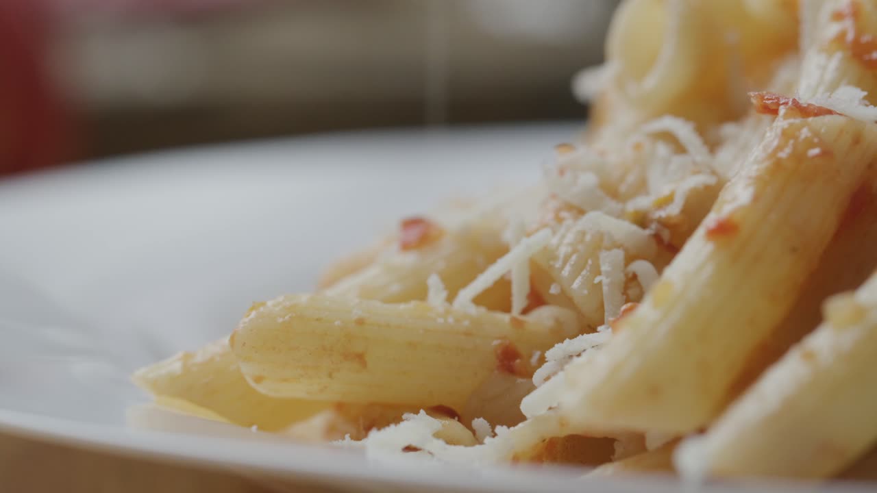 Sprinkling Grated Cheese over Penne Pasta with Tomato Sauce on Plate