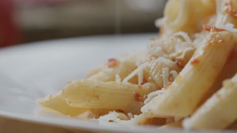 sprinkling grated cheese over penne pasta with tomato sauce on plate