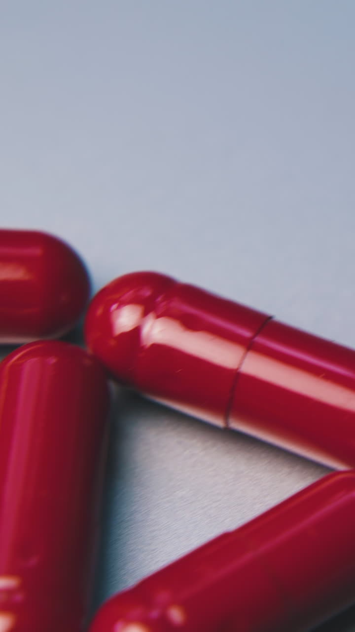 motion past five bright red medical capsules lying on clean white surface extreme close view