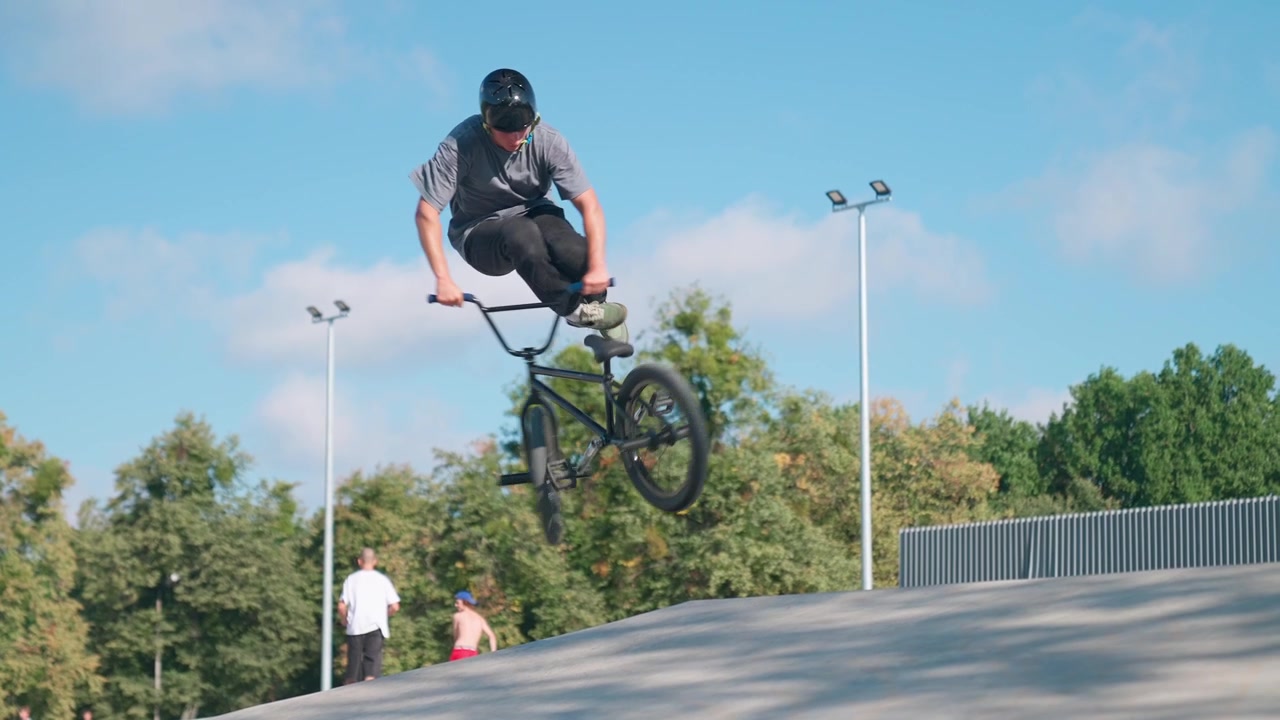Ung mand på BMX-cykel udfører et springtrick i en skatepark
