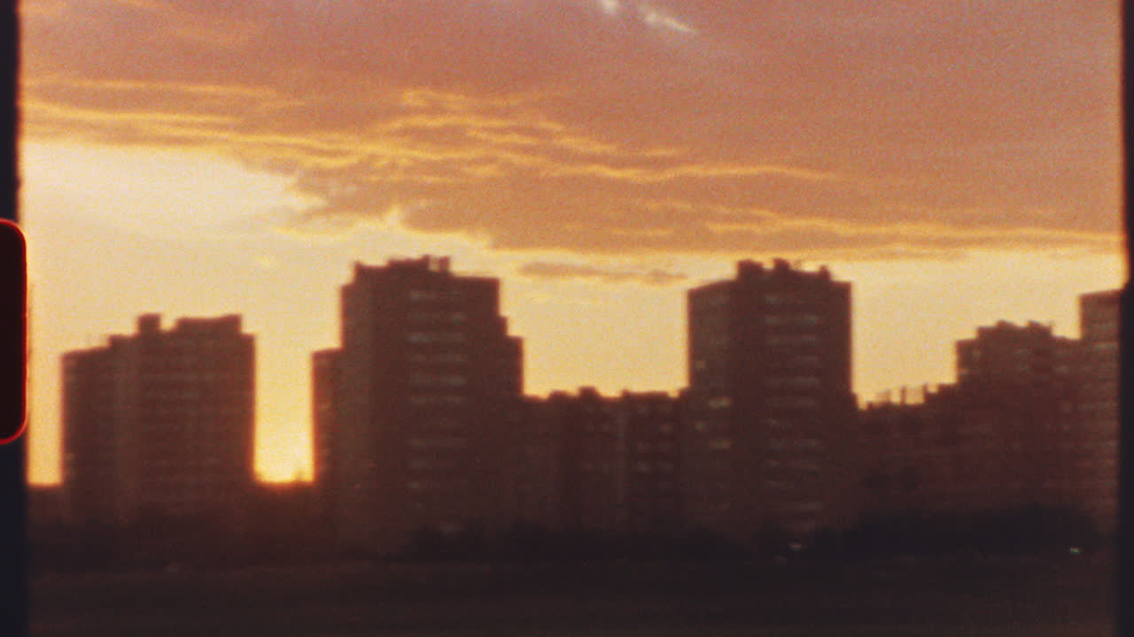 8 mm film - warm sunlight bathing residential buildings in golden hues, casting vibrant orange glow across urban landscape during serene evening twilight with peaceful cityscape atmosphere